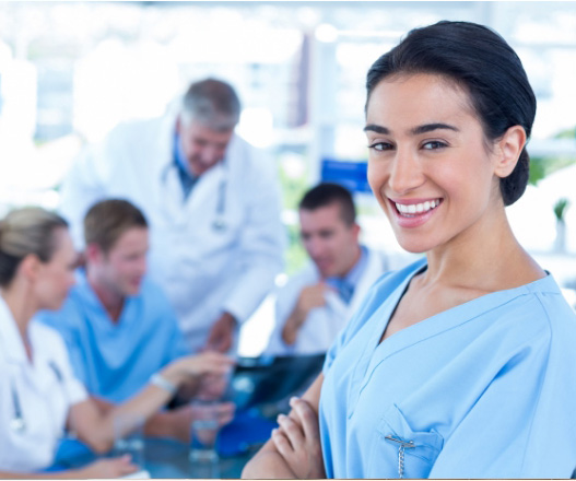Junge Ärztin in blauer Arbeitskleidung lächelt, während ein Team im Hintergrund diskutiert